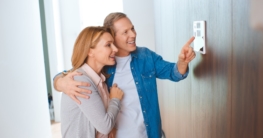 happy man pointing at smart home control panel while hugging wife